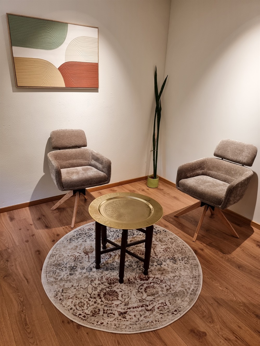 Behandlungsraum mit zwei Sesseln, Tisch auf rundem Teppich und Wandbild